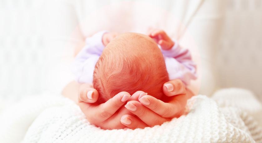 Unas manos de mujer sostienen amorosamente la cabeza de un recién nacido